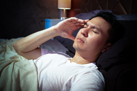 asian man in bed suffering insomnia and headache, thinking about his problem at night