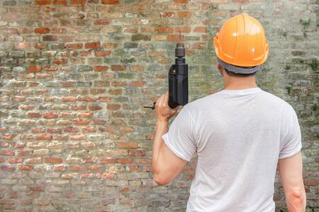 back of asian handyman holding electric drill on old grunge brick wall background. home renovation conceptの写真素材