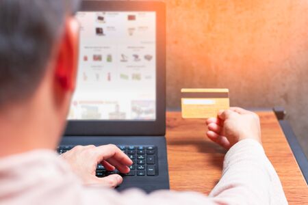 back of male consumer holding credit card for online shopping on laptop computer. e-commerce conceptの写真素材
