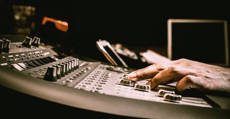 sound engineer hand adjusting audio level on digital mixing console fader in recording, broadcasting studioの写真素材