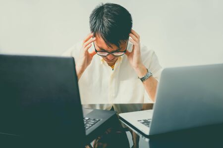 stressful day at the office. young asian businessman holding hands on his face while sitting at the deskの写真素材