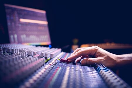 male producer, sound engineer hands working on audio mixing console in broadcasting, recording...
