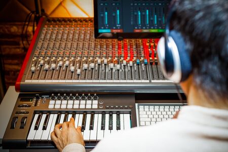 back view of male music producer arranging a song on midi keyboard in home recording studio
