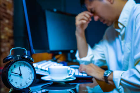 headache, tense young asian businessman working on computer at nightの写真素材