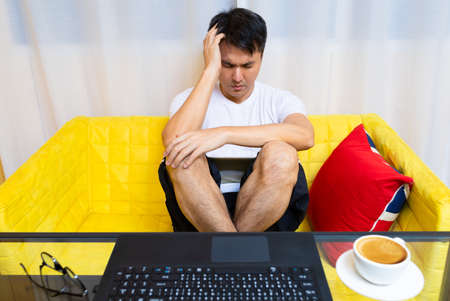 headache, tense young asian man working on laptop computer in living room at nightの写真素材