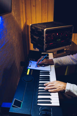 male songwriter playing electric piano and writing a song in home studio at night