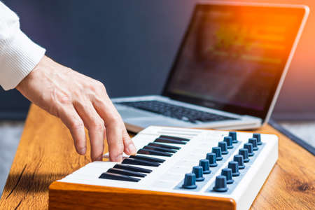 male producer, musician hand playing midi keyboard for arranging a song on laptop computer in home...