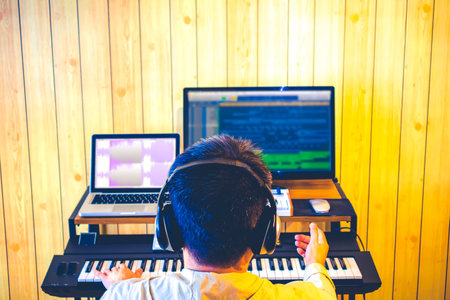 back of asian male music producer arranging a song on computer in home studioの写真素材