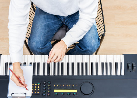 top view of male amateur songwriter playing electric piano and writing a song on white paperの写真素材