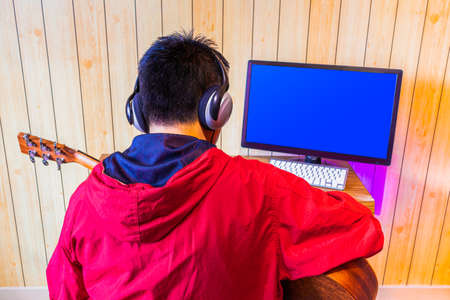 back of asian teenager enjoy learning online guitar lesson from internet in living room