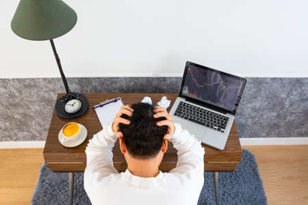 A tense young asian man working on laptop computer in living room at nightの写真素材