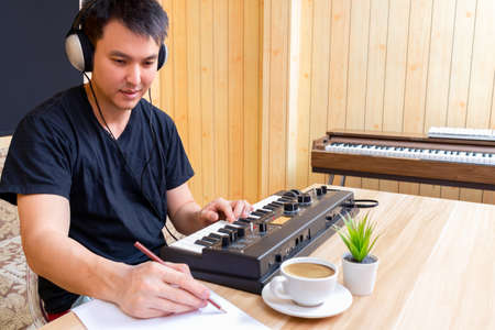 asian handsome male songwriter enjoy writing a hit song while playing music keyboard in living room....