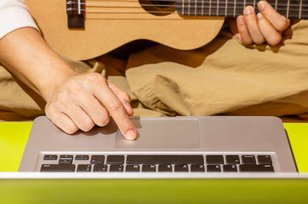 male hand controling mouse point on laptop computer touchpad for learning guitar lesson on internet. e-learning technology conceptの写真素材