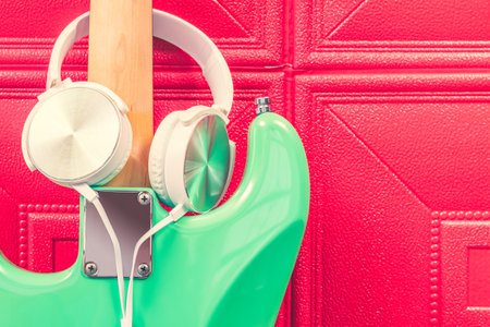 white headphone on green electric guitar neck against red wall. music background