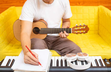male amateur songwriter writing a hit song on white paper while playing acoustic guitar in living room. song writing conceptの写真素材