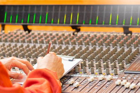 male songwriter hand writing a song on audio mixing console in recording studio. songwriting concept