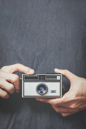 close up male hands holding retro camera and pressing shutter button on black shirt backgroundの写真素材