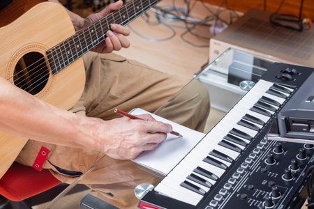 male composer writing a song on paper while playing acoustic guitar in home studio. songwriting or...