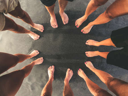 Family picture, all feet together on a beach with black sand. Top view of a group of people standing in a circle barefoot. Mother, father and sons enjoying summer holiday. Togetherness, unity conceptの写真素材