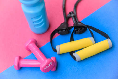 Still life view of fitness object over a colorful background. Weights, elastic rope and water bottle...