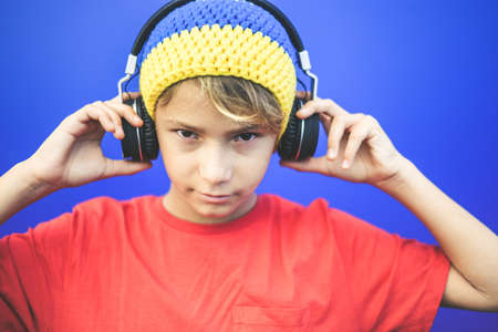 Portrait of a beautiful boy listening music with headphones isolated on a blue background. Colorful...