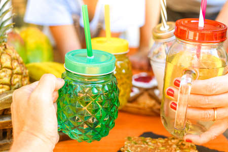 Hands toasting with natural drinks in colorful glasses with straws. Wooden table with natural food, in the background for a healthy and nutritious breakfast. Vegan, vegetarian, bio, diet, meal conceptの写真素材