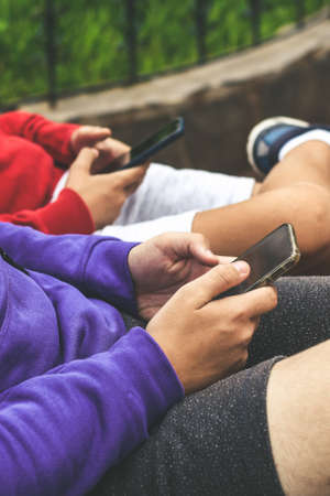 Close up view of a couple of teen using smartphone sitting outdoor at the park. Teenagers communicate with new technology devices with remote friends. Youth, new tech trend and communication concept.の写真素材