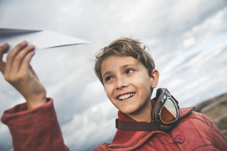 Little boy playing with a paper plane in a sunny day, dreaming about being an airplane pilot and smiling at the camera. Young and happy child with blonde hair thinking about planes and pilots.の写真素材
