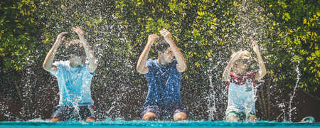Smiling teenagers splash water with their hands. Young male enjoying days off of school relaxing in the swimming pool. Happy people enjoy summer holiday together Youth carefree relax happiness conceptの写真素材