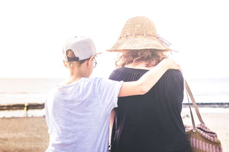 Trendy young mother having fun with her child in summer sunny evening at the beach. Son embracing...