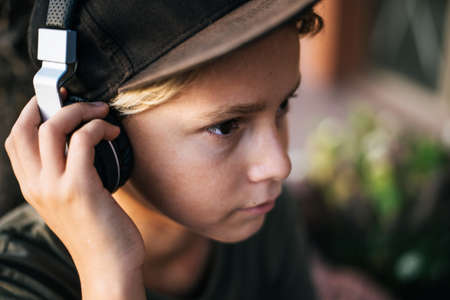 Portrait of a beautiful trendy boy with headphones relax listening music. Close up view of a young male enjoy free time outdoor on a summer evening. Teen enjoying sound. Youth, recreation, fun concept.の写真素材