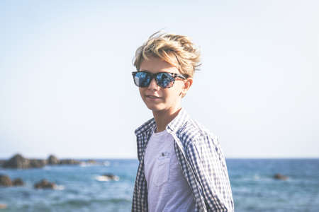 Portrait of a trendy boy smiling at the sea. Beautiful blonde child enjoying summer holidays ready to go to the beach. Cheerful young tourist enjoy summer lifestyle. Youth, happiness, carefree conceptの写真素材