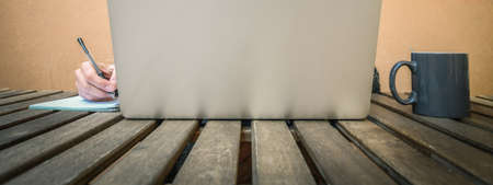 Panorama image of a woman working at desktop using modern technology online. Girl works at home in terrace writing on wooden table with notepad and a cup of coffee. People works and studying outdoorの写真素材