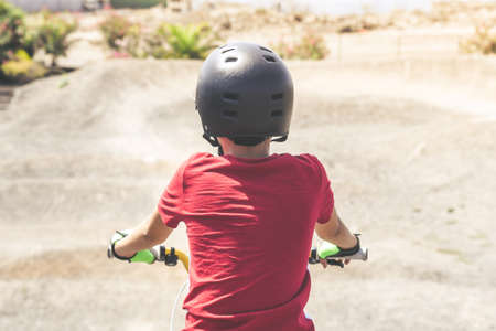 Back view of a young cyclist with bmx ready to start. Young boy wearing helmet riding a bicycle looking the race track. A child having fun outdoor in the park on a summer day. Safety, youth, concept.の写真素材