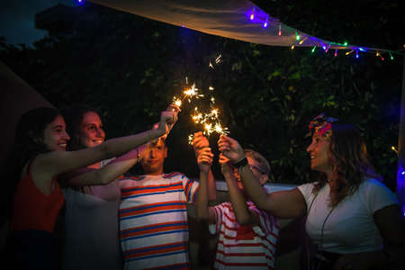 Group of various people making party with fireworks outdoor in terrace. Smiling girls and boys...