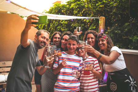 Happy friends taking photo with smartphone at barbecue party. Young people doing appetizer outdoor...