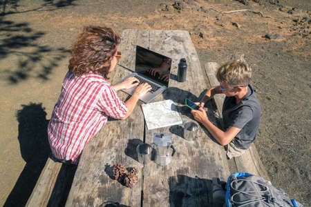 Top view of mother and son taking a rest after mountain trekking. Mum working with laptop Trendy...