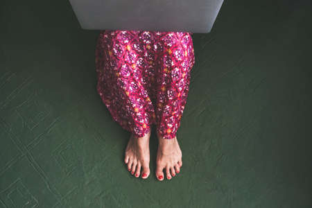 Top view of trendy girl sitting on green vintage floor. Barefoot woman with red nails working with laptop. Woman do shopping online at home Female relax reading a blog New trends technology conceptの写真素材