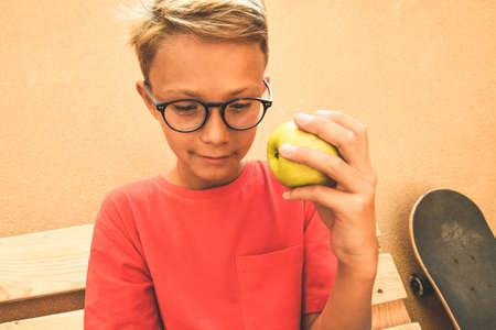 Happy trendy student taking a break and eat a fruit Healthy snack after school at home. Young skater boy doing breakfast meal. Youth lifestyle millennials generation health food positive conceptの写真素材