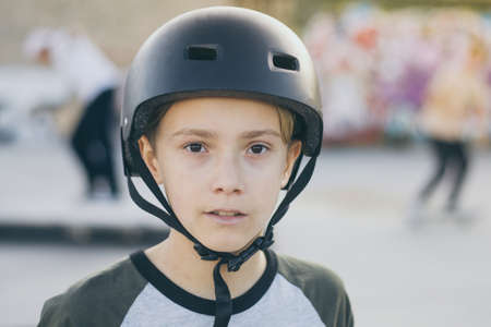 Portrait of trendy young skater at the skatepark wearing helmet, looking in camera. Teenager enjoying sunny day outdoors in the city with skateboard. Youth, happiness, safety, sport, positive conceptの写真素材