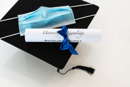 Closeup of graduation hat with degree and surgical mask on white background. On line virtual...
