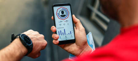 Close up of male hands using fitness app on smartphone. Man resting after jogging reading run results. Running man with Mobile phone connected to a smart watch recording data about sport activity.の写真素材