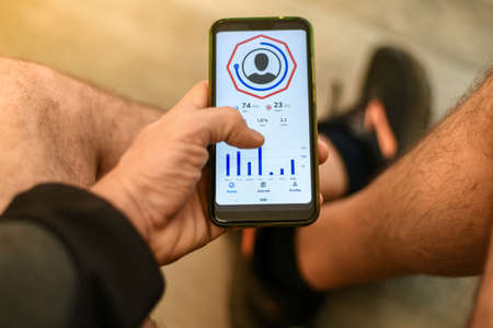 Close up of male hands using fitness app on smartphone. Man resting after jogging reading run results. Running man with Mobile phone connected to a smart watch recording data about sport activity.の写真素材