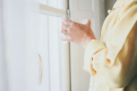 Young woman drinking a cup of tea looking outside the window. Closeup portrait of a girl enjoying...