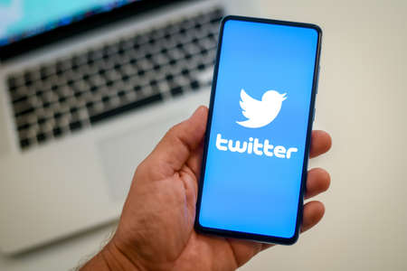 Close up view of hand with smartphone and Twitter logo on display. Laptop on background. New technology, social media, network, communication, concept. Milan, Italy - October 2021のeditorial素材