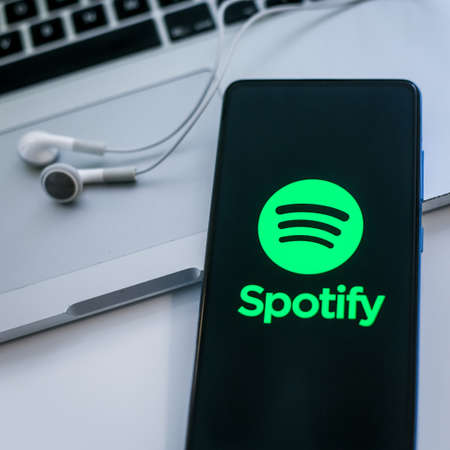 Close up view of a smartphone with Spotify logo on display. Laptop and headphone on background. New technology, social media, network, liquid music concept. Squared image. Milan, Italy - October 2021のeditorial素材
