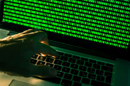 Hand typing on laptop keyboard, green numbers on display. Hacker forcing the system. Programmer...