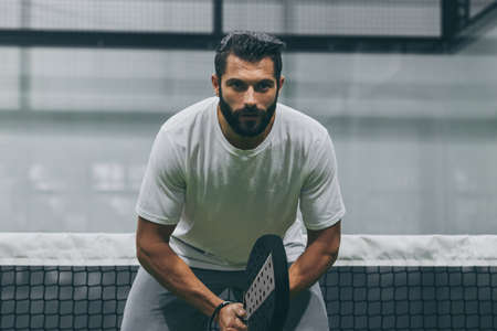 Beautiful man playing paddle tennis, racket in hand concentrated look. Young sporty boy ready for the match. Focused padel athlete ready to receive the ball. Sport, health, youth and leisure conceptの写真素材