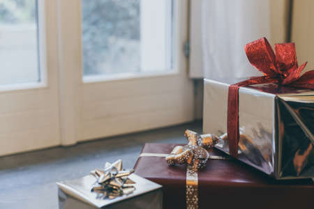 Christmas gift boxes on floor near the door inside home. Box with holiday ribbon with bows. Warm festive family atmosphere. New year, happiness, togetherness, holidays, surprise, e-commerce conceptの写真素材