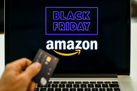 Hand with credit card in front of the laptop monitor doing purchases Amazon on line shop black...